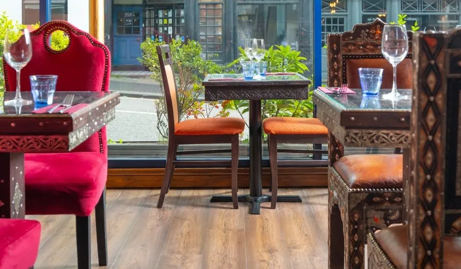 A window-side table at Al Farid, set with glasses beside carved Moroccan chairs and red velvet seating, the St Albans street beyond